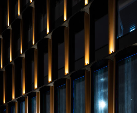 Architectural detail of a modern facade at night. A rhythmic pattern of illuminated columns contrasts with dark reflective windows, creating a sleek corporate background.