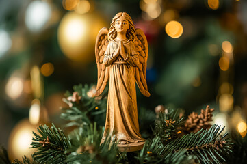 A wooden statue of an angel placed on an ornamented Christmas tree.