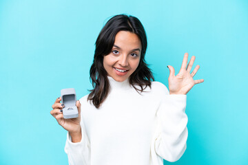Fototapeta premium Young hispanic woman holding a engagement ring isolated on blue background counting five with fingers