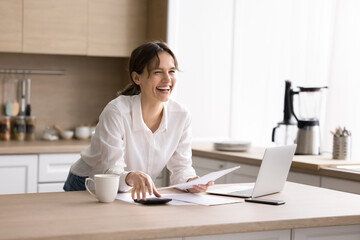 Joyful excited young lady laughing distracted from domestic bookkeeping paperwork