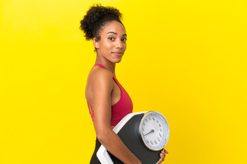 Young African American woman isolated on yellow background with weighing machine
