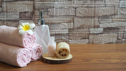 Spa composition with rolled pink towels, plumeria flower, liquid soap dispenser, and natural loofah on wooden table. Perfect for relaxation, wellness, and beauty treatment concepts.