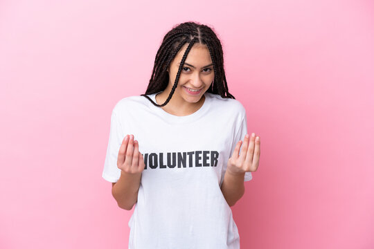 Teenager volunteer girl with braids isolated on pink background making money gesture