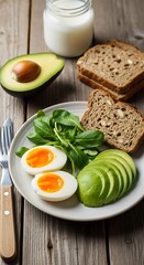 Healthy breakfast plate with soft-boiled eggs, sliced avocado, fresh greens, whole grain bread, and milk on a rustic wooden table.