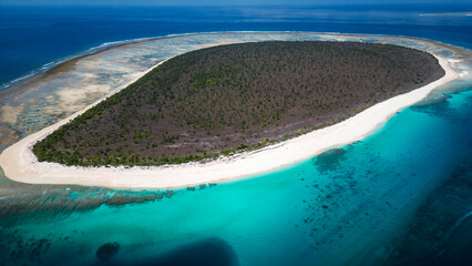 Stunning high-angle view of an exclusive tropical resort situated on a crescent-shaped white sand beach. The clear turquoise water of the lagoon meets the deep blue ocean horizon. Traditional thatched