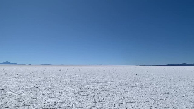 Window view during ride in offroad vehicle: extreme conditions form salt crust on surface of Salar de Uyuni salt flat as a result of salt crystallization from evaporating water. Andean mountain ridge.