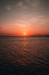 Naklejka premium Stunning sunset paints the ocean with fiery orange hues reflecting on calm water, creating a serene and majestic coastal panorama.