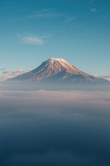 Fototapeta premium Majestic snow-capped mountain peak emerges from a sea of soft clouds under a clear blue sky, inspiring awe and adventure.