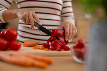 Woman preparing fresh vegetables slicing red pepper on cutting board