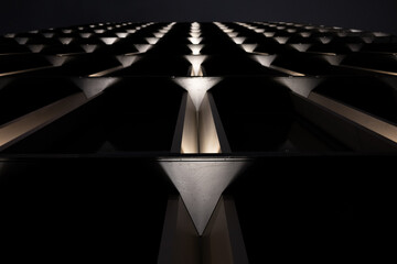 Low angle view of a modern building facade at night. The symmetrical, illuminated patterns create a futuristic and abstract architectural background with a strong sense of perspective.