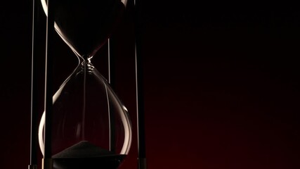 macro video showing sand streaming through a glass spinning hourglass in front of black background - Powered by Adobe