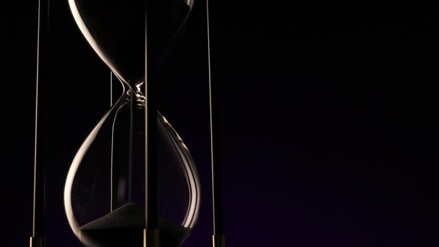 dark hourglass with fine sand flowing, a metaphor for the irreversible passage of time and life�s fragile continuity.