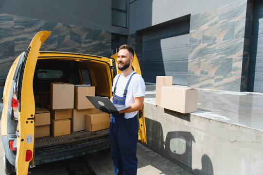 Deliveryman holding laptop next to van full of cardboard boxes