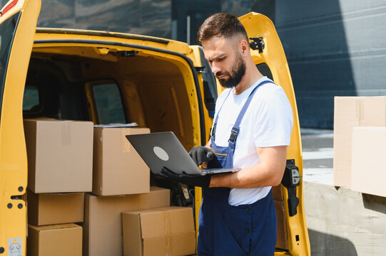Deliveryman using laptop next to van full of cardboard boxes