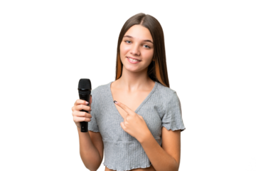 Teenager singer girl picking up a microphone over isolated background pointing to the side to present a product