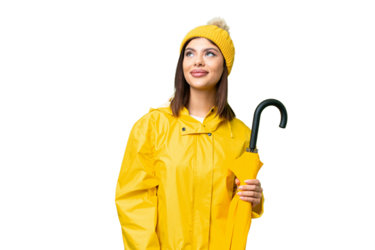 Young Russian woman with rainproof coat and umbrella over isolated chroma key background thinking an idea while looking up