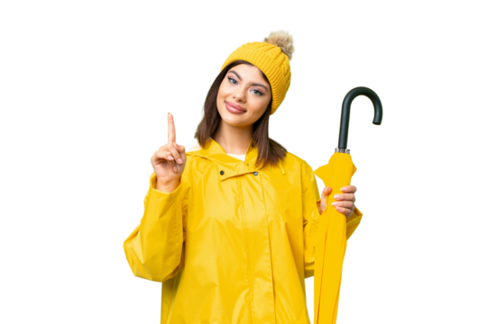 Young Russian woman with rainproof coat and umbrella over isolated chroma key background showing and lifting a finger in sign of the best