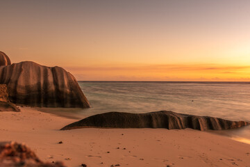 Romantic sunset at Anse Source d’Argent, with golden light reflecting on the turquoise water, iconic granite boulders, and a dreamy tropical beach setting