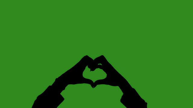 A black silhouette of female hands shows a heart sign with fingers in close up on a green chroma key background. Minimalist contrast and modern visual composition, mockup.
