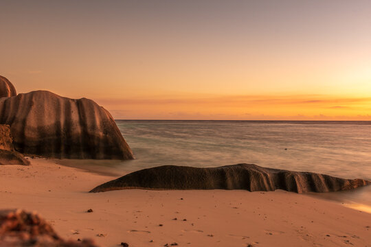 Romantic sunset at Anse Source d&rsquo;Argent, with golden light reflecting on the turquoise water, iconic granite boulders, and a dreamy tropical beach setting