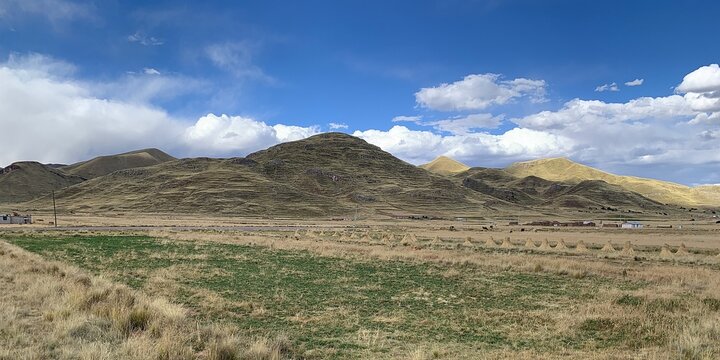 Puno, Peru: Panoramic view over Altiplano landscape to grassy hill with terraces in the Andean highlands. Clouds seem to hang low because of great elevation. 