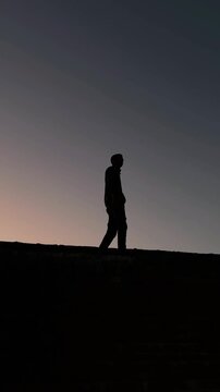 Silhouette Man Walking on Bridge Captured from Below During Sunset