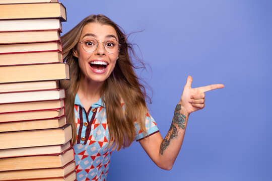 Young woman with stack of book smiling and pointing against purple background