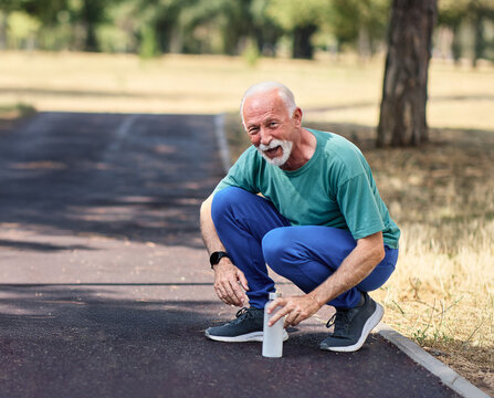 Smiling active mature elderly man jogging running and holding a water bottle in the park