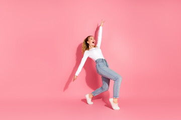 Young woman in casual style posing playfully against a pink background, showcasing trendy fashion...