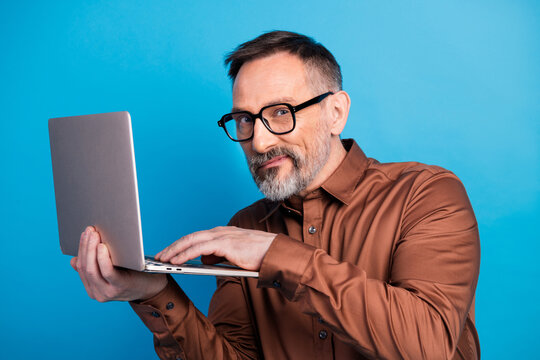 Businessman using a laptop against a blue background smiling and confident executive portrait in formal shirt and glasses