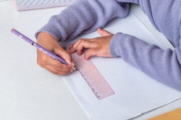 A little girl drawing on paper using pencil and ruler
