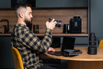 Young bearded content creator, a professional photographer or videographer, works from home, checking his camera gear with a laptop and drone.