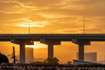 Naklejka premium Golden sunset over urban bridge and highway pillars at dusk with silhouetted city