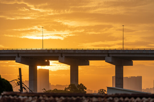 Golden sunset over urban bridge and highway pillars at dusk with silhouetted city