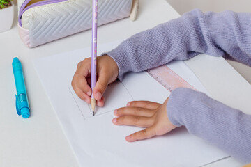 A little girl drawing something on paper using a pencil on the table
