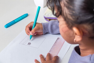 A little Asian girl drawing using a pen on a table