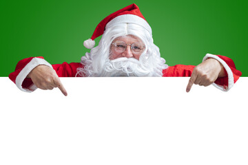 Naklejka premium Santa Claus Pointing at Blank White Sign on Green Background for Christmas Holiday Promotions and Advertising