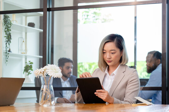 asian businesswoman in formal suit sitting at coworking space in green office, group of multiracial team colleague diverse employee coworker meeting at environment sustainable workplace