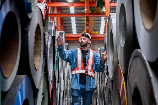 man engineer worker check and inspect material stainless galvanized metal sheet roll in warehouse, group of people in safety vest and helmet working together at industrial manufacturing