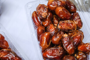 Close-up of fresh dates piled in a clear plastic container on a white surface with warm lighting.