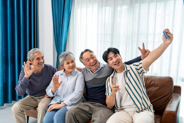group of asian senior and son selfie video call using mobile phone waving hands and smiling for healthy longevity lifestyle. elderly people family greeting celebrate festive holiday together at home