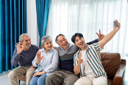 group of asian senior and son selfie video call using mobile phone waving hands and smiling for healthy longevity lifestyle. elderly people family greeting celebrate festive holiday together at home