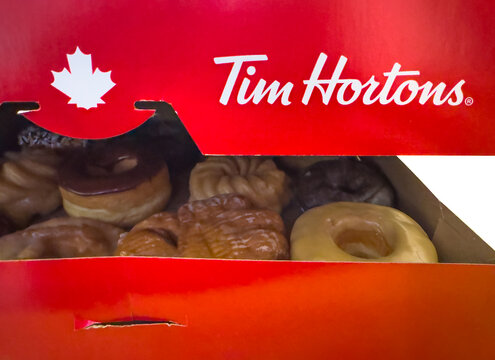 Calgary, Alberta, Canada. Nov 8, 2025. Open Tim Hortons box with assorted donuts: chocolate-glazed, cruller, honey dip and maple-glazed displayed inside a red branded box.
