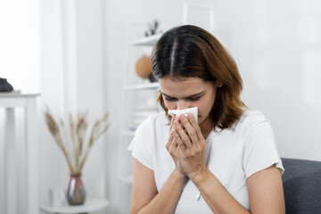 women using tissue to blow her nose at home. Concept of seasonal allergies, cold, flu or respiratory illness. Indoor healthcare and sickness prevention in daily life.