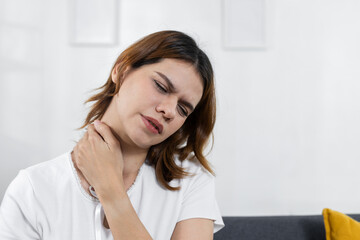 women suffering from neck pain at home, touching her neck with discomfort. Concept of muscle strain, bad posture, stress or physical health issues in daily life.