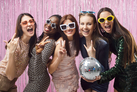 Positive stylish women enjoying disco party, holding shiny disco ball celebrating something, exclaiming and showing peace gesture, being very happy, spending free time together, having fun