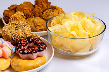 Close-up of donuts, fried potato chips and fried chicken on plate in tudio shot.