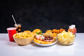 French fries, burgers and other fast food on plate on wooden table against black background, studio shot, unhealthy fast food