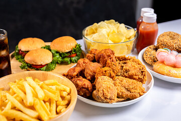 Close-up of unhealthy fast food, hamburger, fried chicken, donuts and french fries on plate.