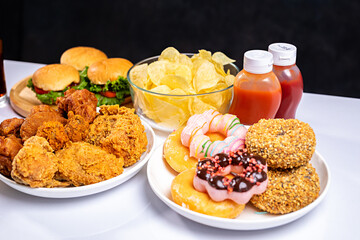 French fries, burgers and other fast food on plate on wooden table against black background, studio shot, unhealthy fast food
